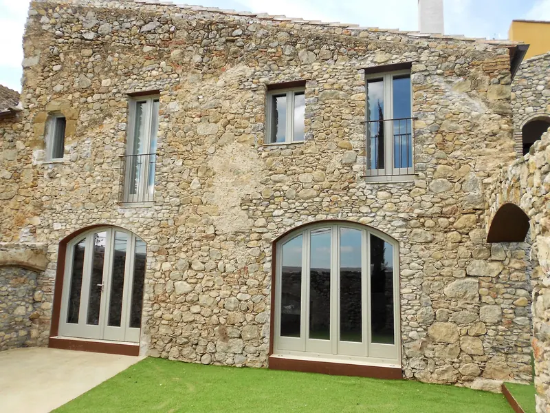 Façana de pedra rehabilitada amb finestrals d’arc de mig punt i gespa al davant