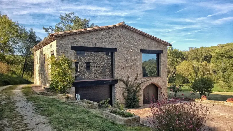Masia de pedra rehabilitada amb finestres de marc fosc, envoltada de camps i arbres