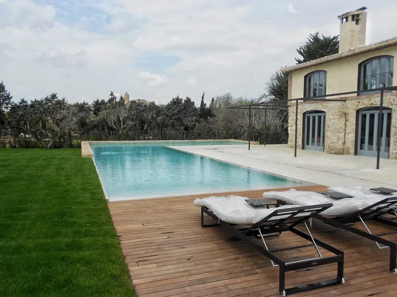 Piscina allargada amb solàrium de fusta i gandules davant d’una casa de pedra